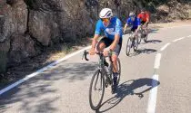 Three cyclists riding along open roads next to mountains in the sun