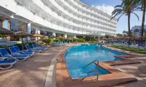 Mallorca 312 Hotel featuring a while building with balconies, a pool, deck chairs and pam trees all under a blue sky. 