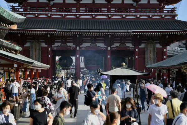 A wide-angle view of Senso-ji Temple in Asakusa, Tokyo, featuring the iconic red Kaminarimon gate with its large hanging lantern, bustling with visitors and framed by traditional architecture and colourful shops along Nakamise Street.