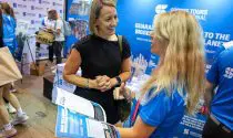 Sports Tours International representative speaking to another women at a running exhibition. With a Sports Tours International branded back drop and table in the background.