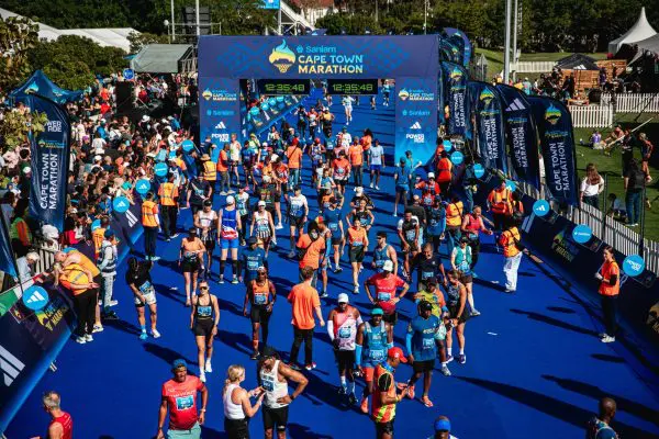 Runners participating in the Sanlam Cape Town Marathon crossing the finish line on a blue carpet underneath a Cape Town Marathon blue archway