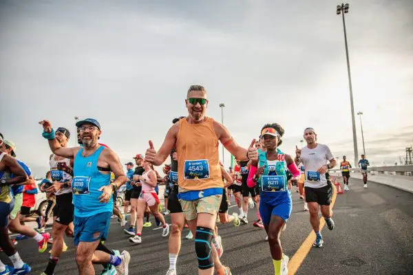 Runners participating in the Sanlam Cape Town Marathon, a male runner with sunglasses in the centre, with his thumbs up and smiling to the camera