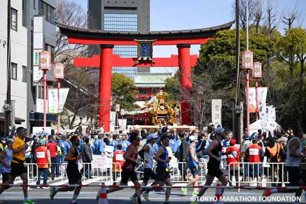Runners passing a cheer zone at the Tokyo Marathon with the Tomioka Hachiman Shrine in the background