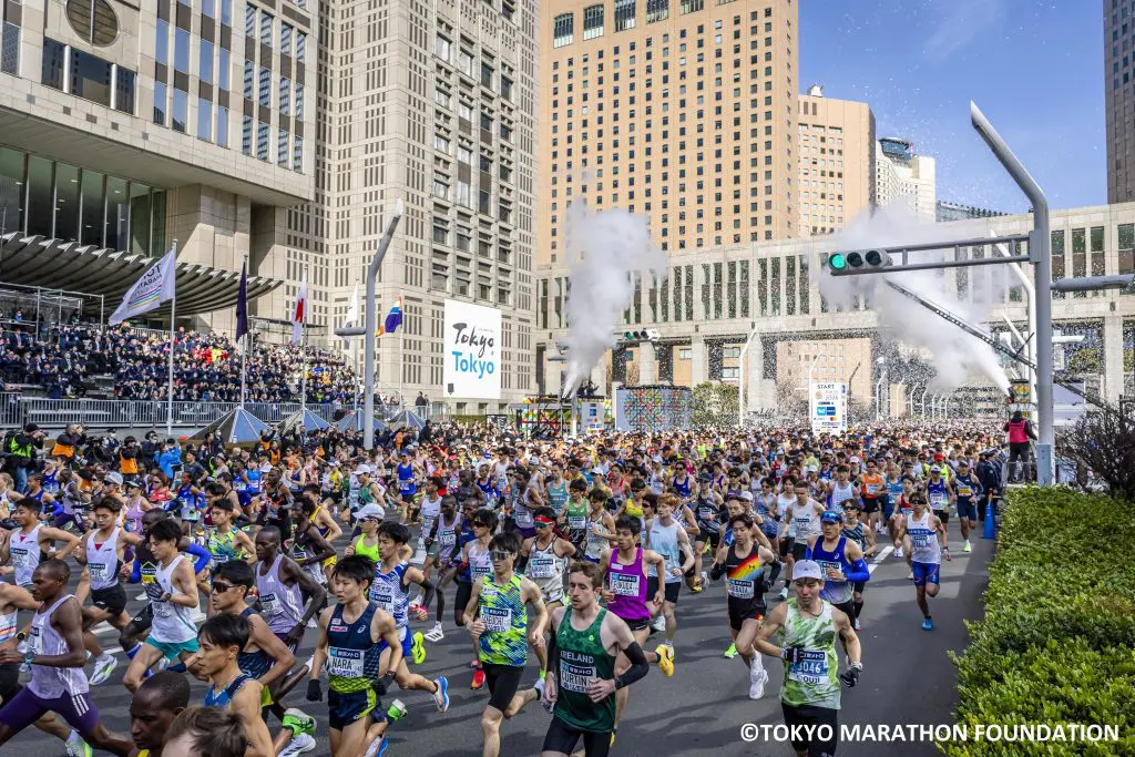 Runners crossing the start line of the Tokyo Marathon, in Japan. With white confetti and smoke in the air as a signal for the runners to begin.